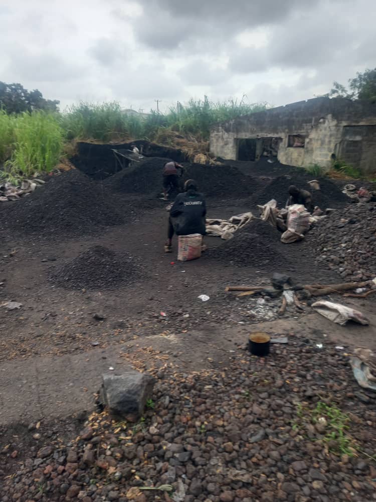 Dark ore stockpiles at a working site, with sacks and a low building beyond