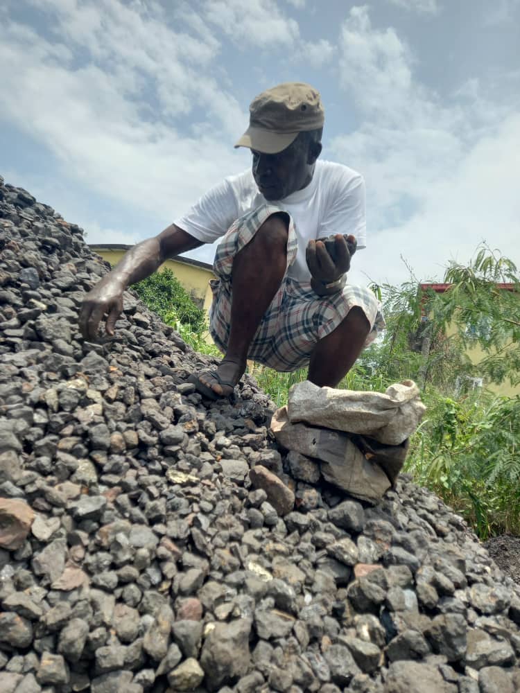 A man crouching on crushed dark ore and inspecting a piece by hand