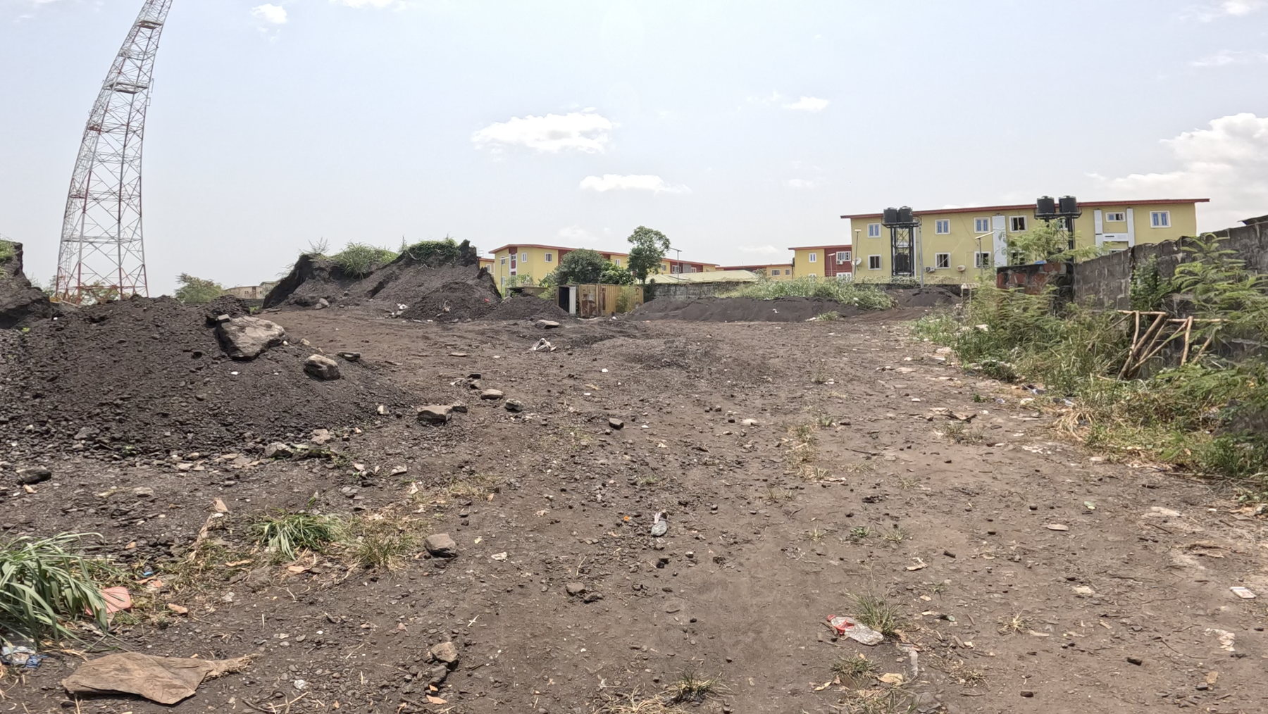 Dark spoil heaps across an open yard, with low buildings beyond