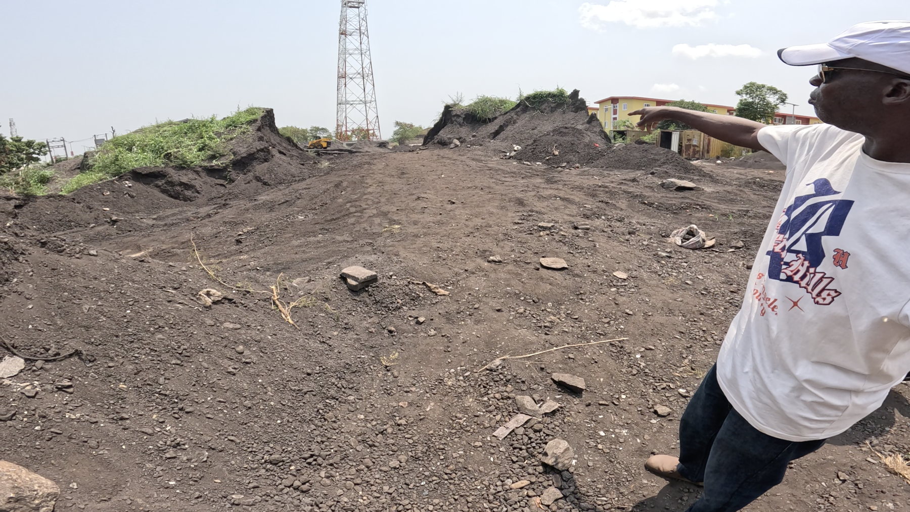 Worked dark ground between spoil heaps, with a man indicating the yard